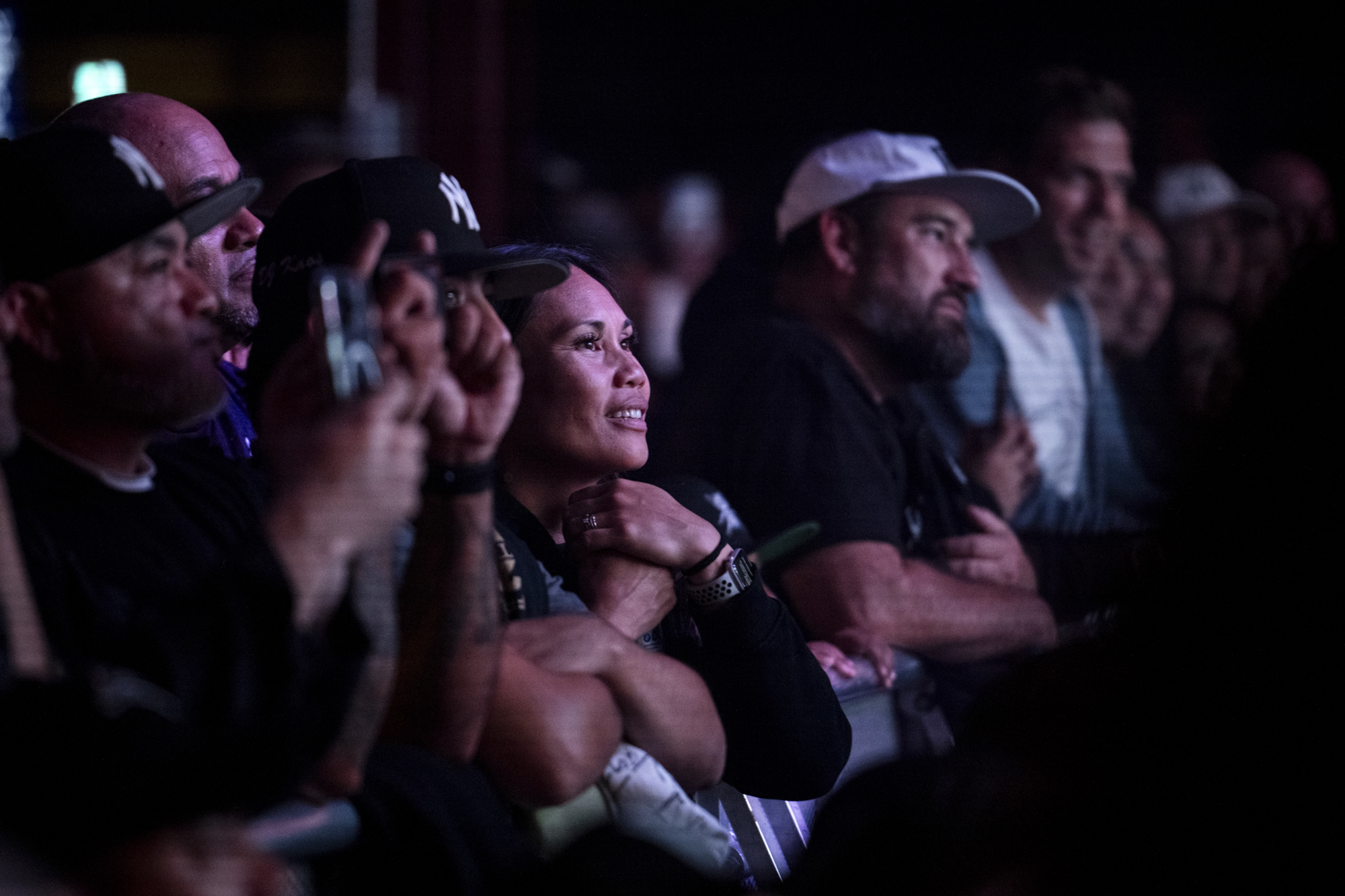 People stand in a crowd leaning on a barrier indoors.