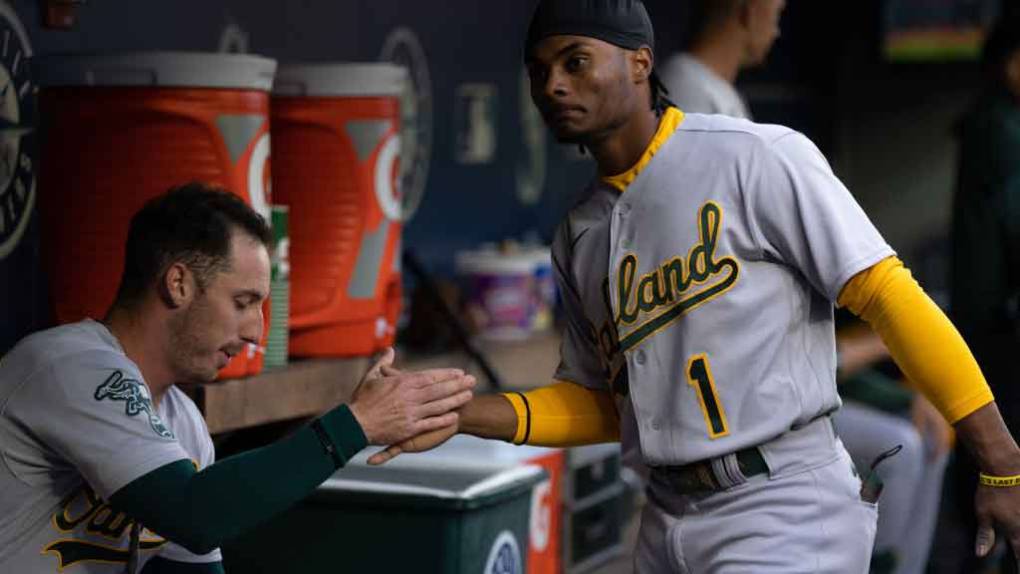 Two baseball players slap hands in a dugout with orange Gatorade jugs in the background.