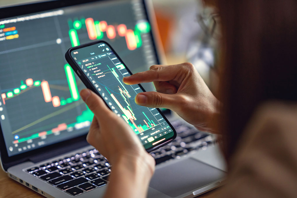 Woman checking Bitcoin price chart on digital exchange on smartphone and a laptop