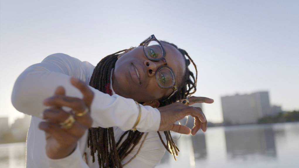 A close-up of a woman looking into the camera while practicing capoeira moves by Lake Merritt in Oakland, CA