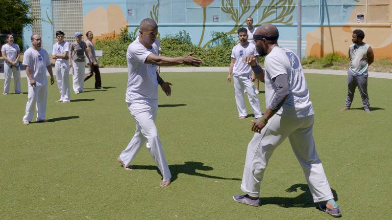 A group of men is standing on a field and is about to play capoeira.