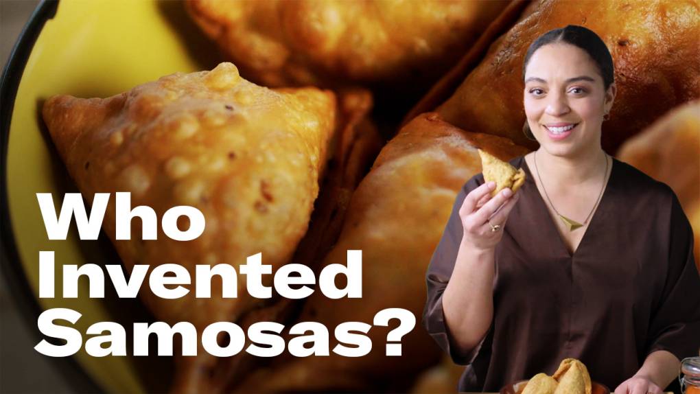 A smiling woman holding a samosa is positioned against a backdrop that is a closeup of a bowl filled with crispy triangular samosas