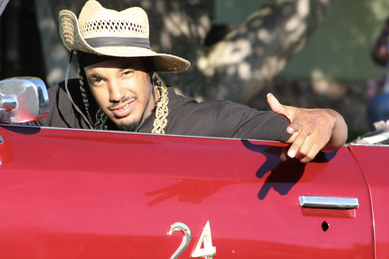 Well-known rapper and proud representative of Pittsburg's El Pueblo Projects, The Husalah, posing for a photo while sitting in a cherry red drop top car.