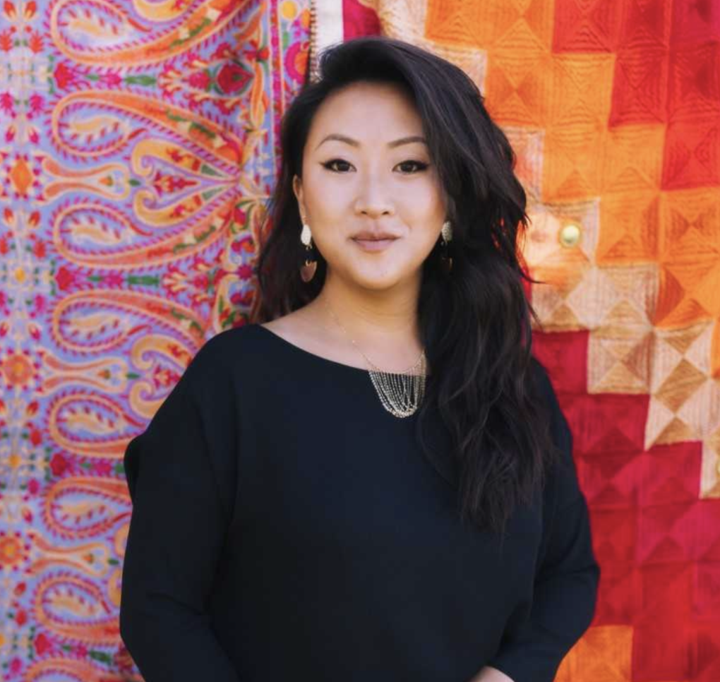 Woman in black clothing poses for a photo in front of a multi-colored background.